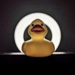 A slightly ominous looking rubber duck sitting in a dark environment with a bright circle of light behind it